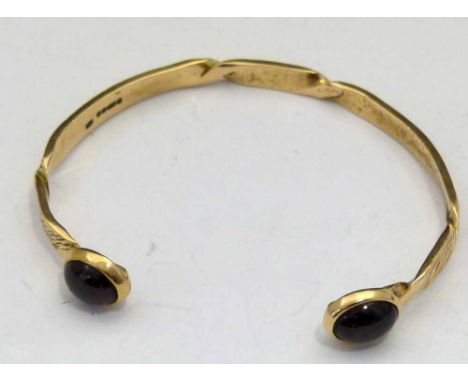 9ct gold slave bangle with two red stone terminals, 12.9g gross.