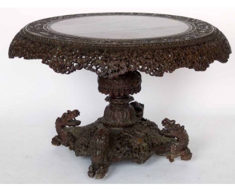 Burmese carved hardwood circular centre table, the tip top with a border of scrolling foliage, pavilions and dragons on an or