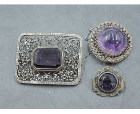 A white metal and amethyst brooch, with central emerald-cut amethyst within a pierced C-scroll surround, unmarked, 5.5cm, sol