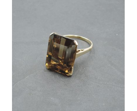 An oversized baguette cut smoky quartz ring having a four claw basket mount on a yellow metal loop stamped 9ct, size N &amp; 
