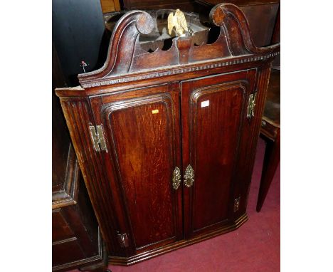 A George III oak double door hanging corner cupboard, having broken architectural pediment and fluted detail