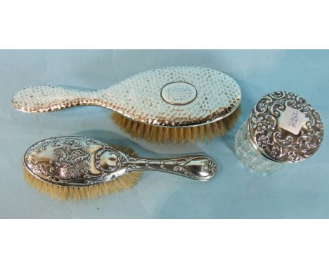 A beaten silver-backed hairbrush, Birmingham 1901, another with raised decoration and a silver topped dressing table jar, Lon