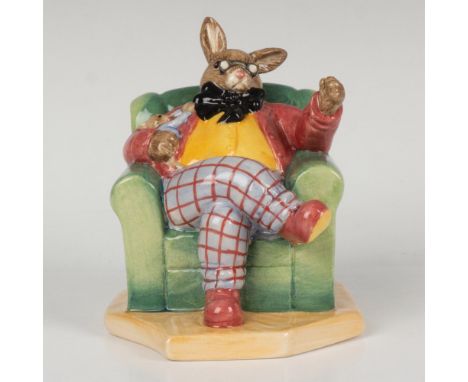 A figure of a bunny sitting in an armchair, telling someone a story. Dressed with a yellow button down, black tire, and check