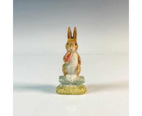 Hand painted figure of a seated brown and white rabbit with feet out, eating a carrot. The figure is inspired by Beatrix Pott
