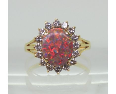 AN OPAL & DIAMOND RING set with an 11mm x 9mm x 1.9mm mainly red blue opal, surrounded with  halo of diamonds with an estimat