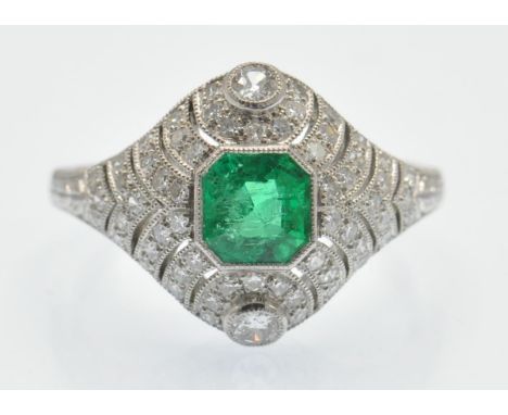 A platinum emerald and diamond dome ring. The ring set with a central emerald within a pierced dome setting having two bezel 