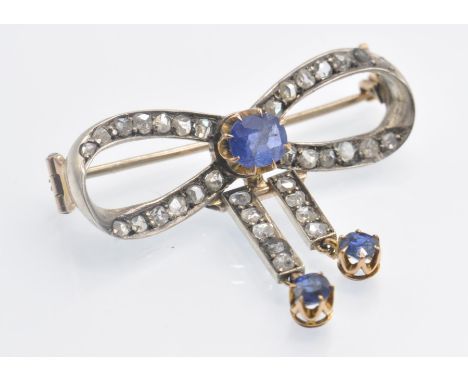 An antique gold sapphire and diamond brooch pin. The brooch in the form of a bow having twin articulating sapphire drops ,sur