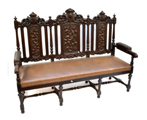 &nbsp;An early 20th century carved oak three seat settee, with foliate detail and light tan upholstery, on stretchered suppor