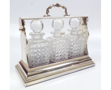 A Betjemann's Patent silver plated three division tantalus with gadrooned detail housing three clear hobnail cut glass decant