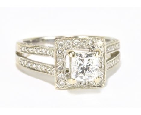 An 18ct white gold and diamond ring, the raised central princess cut stone within a border of twenty round brilliant cut ston