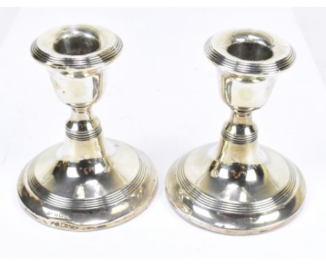 WILLIAM AITKEN; a pair of George V hallmarked silver squat form candlesticks, each with linear decoration, Birmingham 1916 (f