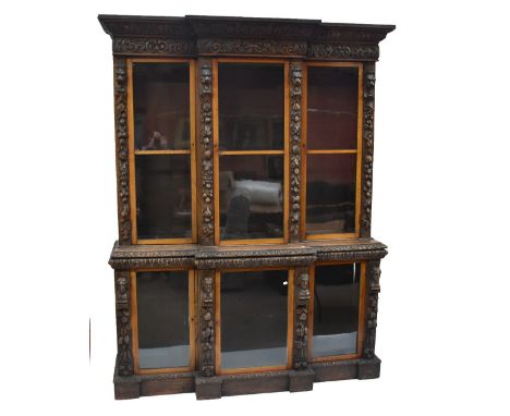 A Victorian carved oak breakfront bookcase, the upper and lower sections each with three glazed doors, with foliate and mask 