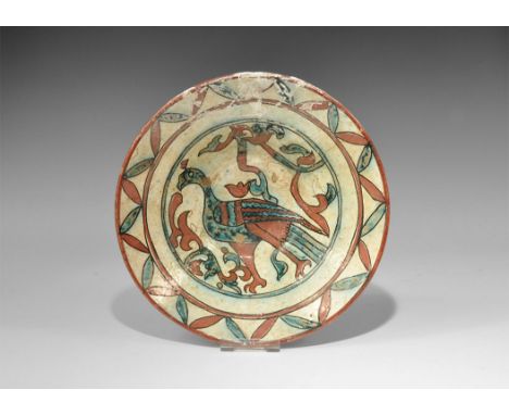 An undated archaistic cream-glazed ceramic bowl with border of red and green foliage, central design of a standing bird amid 