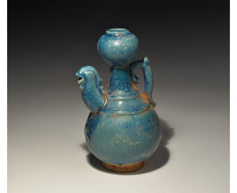 An undated archaistic blue-glazed ceramic jug with tall balustered neck and bulb, scrolled handle with thumb-pad, spout forme