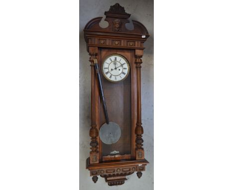A large walnut Vienna-style wall clock, carved broken arch pediment above decorative frieze, white enamel dial set with Roman