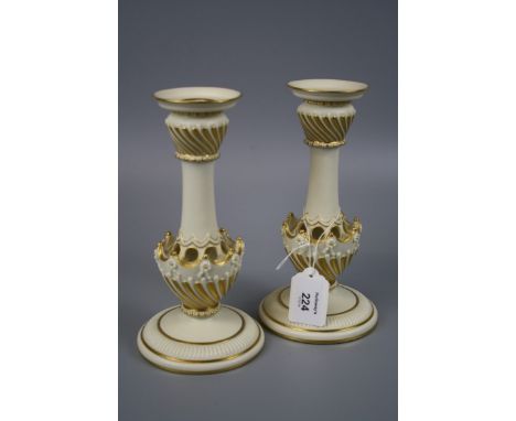 A pair of Royal Worcester ivory and gilt ground table candlesticks, each with gadrooned sconce and pierced column on a domed 