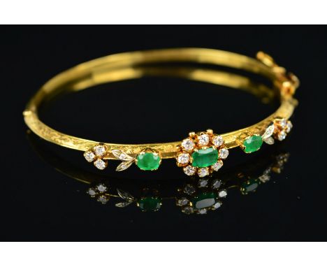 A MID 20TH CENTURY 18CT GOLD EMERALD AND DIAMOND HALF HOOP BANGLE, centring on an emerald and diamond oval cluster, flanked b