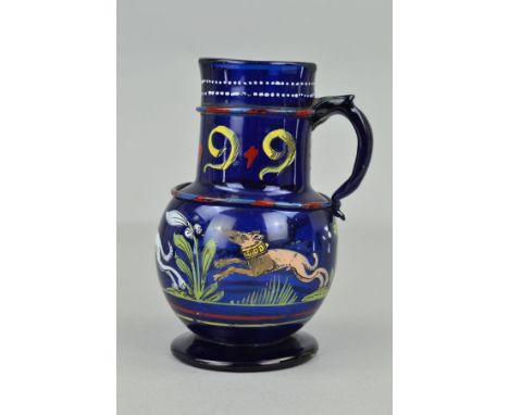 A 16TH CENTURY STYLE BLUE GLASS EWER, the cylindrical neck applied with a band and handle and enamelled 1599, the bulbous bod