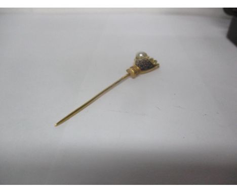 A yellow metal stick pin fashioned as a hand holding a faux pearlLocation: 