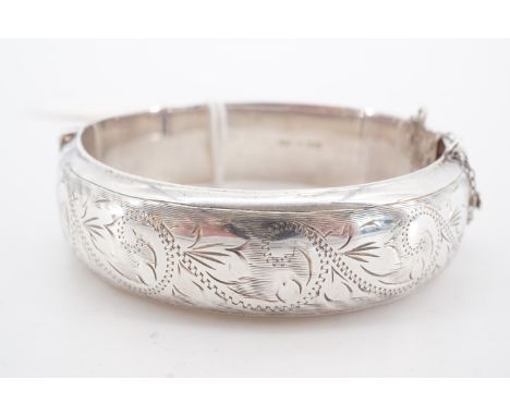 A silver hinged D-section bangle, bearing engraved foliate scroll decoration, Birmingham, 1966