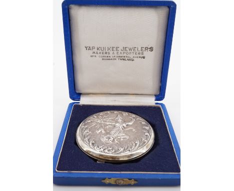 A mid-20th Century Siamese white metal powder compact, the cover repouse worked and engraved in depiction of a deity, in orig