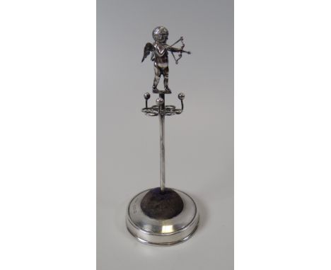 A SILVER 'CUPID' HAT-PIN STAND with pin-cushion, ring tree and hat-pin holder combined, on a circular base and with a figure 