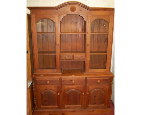 A modern stained pine dresser, having twin glazed upper doors over three frieze drawers to conforming arched recessed panel c