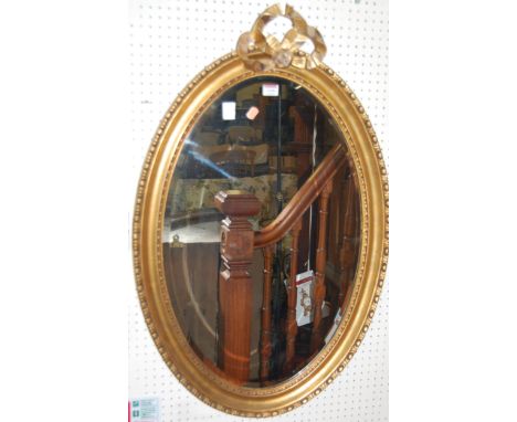 A contemporary gilt and floral bordered oval wall mirror, having removable bow shaped surmount, 92x59cm