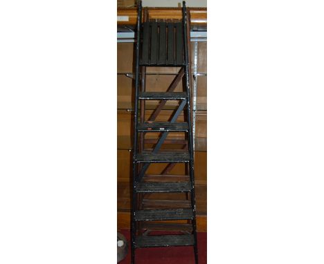 A black painted A-frame decorators ladder, having seven treads; together with a near-matching stained example with seven trea