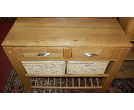 A contemporary light oak two drawer side table, having twin laddered undertiers with two removable wicker baskets, width 110c