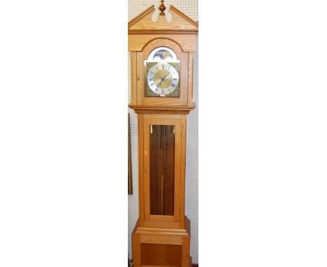 A contemporary light oak long case clock, having an arched silvered and brass moon phase dial, with glazed trunk door and twi