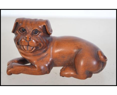 A Japanese fruitwood carved netsuke in the form of a dog signed to the base. Measures 6cm long.