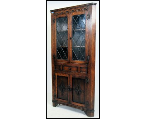 A Jaycee style Jacobean revival corner cupboard having leaded glass doors over carved doors beneath. Shelf lined interior wit