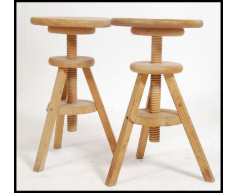 A pair of solid wood retro artists stools having adjustable height seat pads raised on tripod legs. Measures 55cm high x 38cm