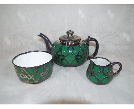 A Royal Worcester Art Silver Work teapot, milk and sugar bowl decorated with applied pierced silver overlay on a green ground