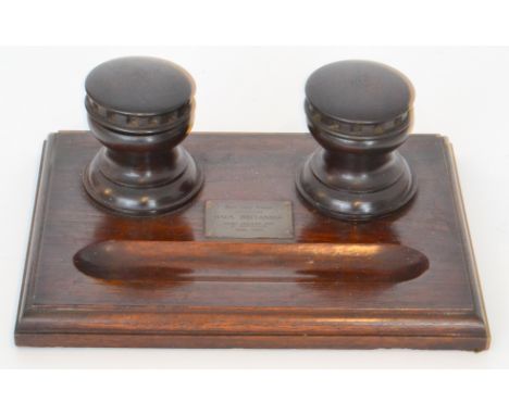 An early 20th Century oak desk stand with castellated turned inkwells with ceramic liners and inset with a brass plaque made 