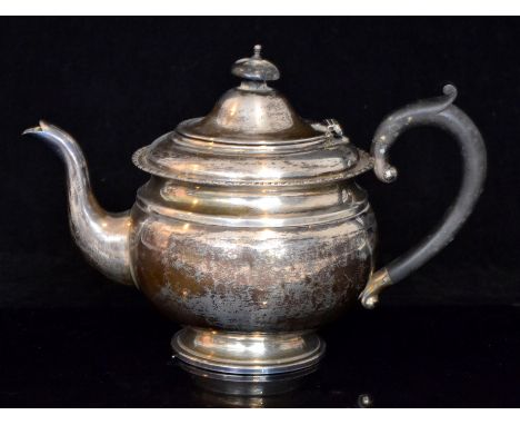 A George V hallmarked silver teapot of squat circular form with beed and reel rim, ebonised scroll handle and raised on circu