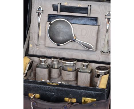 An early 20th Century leather travelling case with six fitted hallmarked silver and tortoise topped glass bottles, a three pi