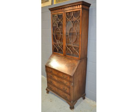 A George III style mahogany bureau bookcase enclosed by a pair of bar glazed doors below a dentil cornice above four long gra