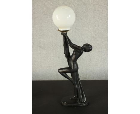 An Art Deco style black resin table lamp in the form of a nude dancer with white glass globe shade. H.70 W.22 D.14cm. 