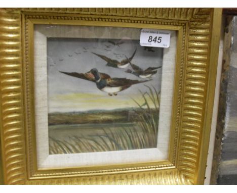 A framed and glazed ceramic tile with hand painted decoration of mallard coming in over reed beds unsigned, inscribed verso "