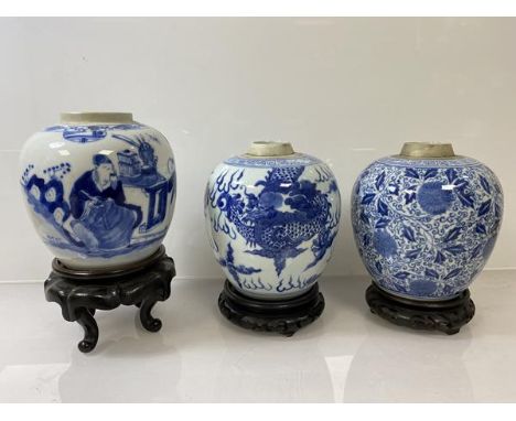 A group of three Chinese ginger jars, all lacking lids, all on carved wooden stands, one depicting scholar, two blue concentr