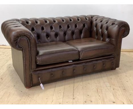 A Chesterfield two seat sofa, upholstered in deep buttoned brown leather, with two squab cushions, raised on compressed bun s