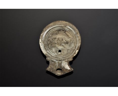 1st century AD. A greyware lamp with broad body and nozzle with volute scrolls; high-relief image of a charging boar to the d