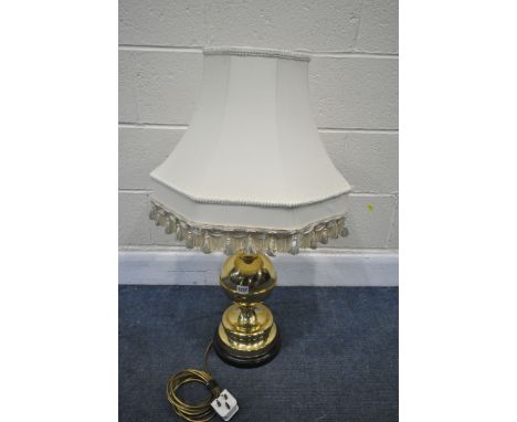 A BRASS TABLE LAMP, with a cream fabric shade, and a bulbous shaft, on a wooden base, height 60cm