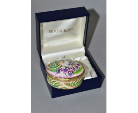 A BOXED MOORCROFT ENAMEL TRINKET BOX, of oval form, decorated in the 'Foxgloves' pattern, with fern inside the hinged lid, pr