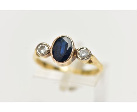 A YELLOW METAL SAPPHIRE AND DIAMOND RING, centering on an oval cut deep blue sapphire, collet set, flanked with two round bri