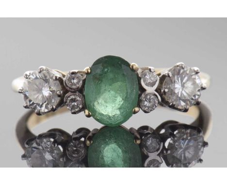 Emerald and diamond ring centring an oval cut emerald, flanked by four small diamonds and two round brilliant cut diamonds, d