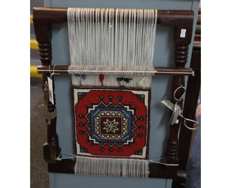 Small turned wooden weaving carpet loom with accessories including scissors etc, with a patterned piece of carpet to the cent