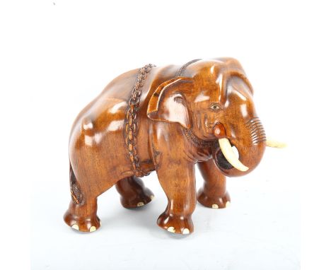 A well carved Indian honey coloured hardwood model of an elephant with chains and ivory tusks, height 17cm, length 21cm 